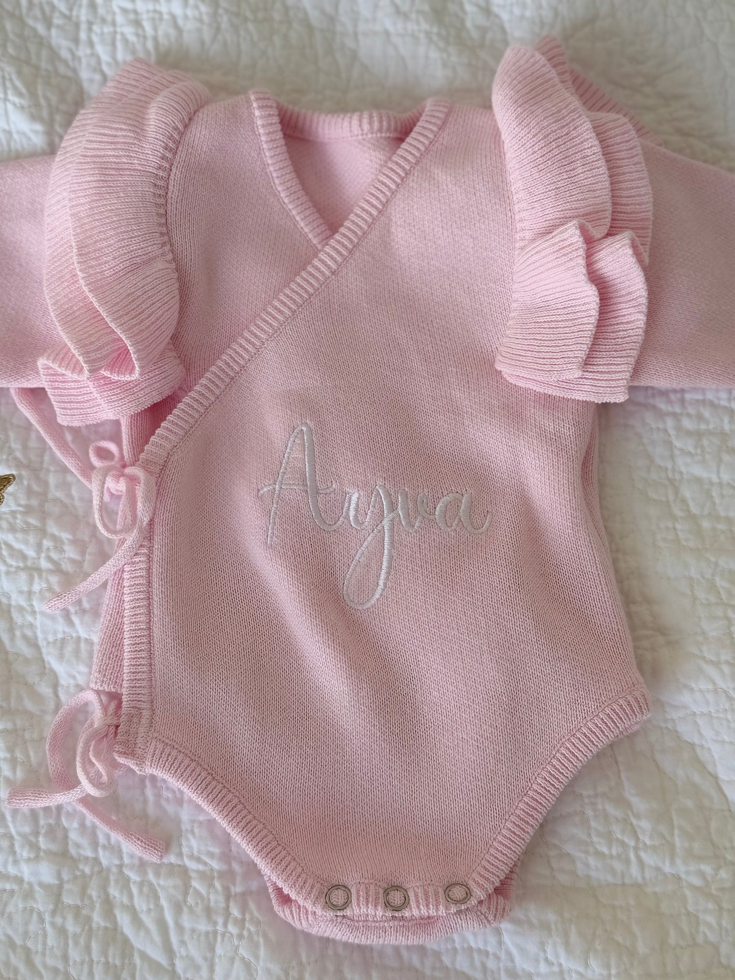 Personalised pink knit baby romper with sweet ruffle sleeves styled on quilt — Maxims Gift Co. nursery gift UAE
