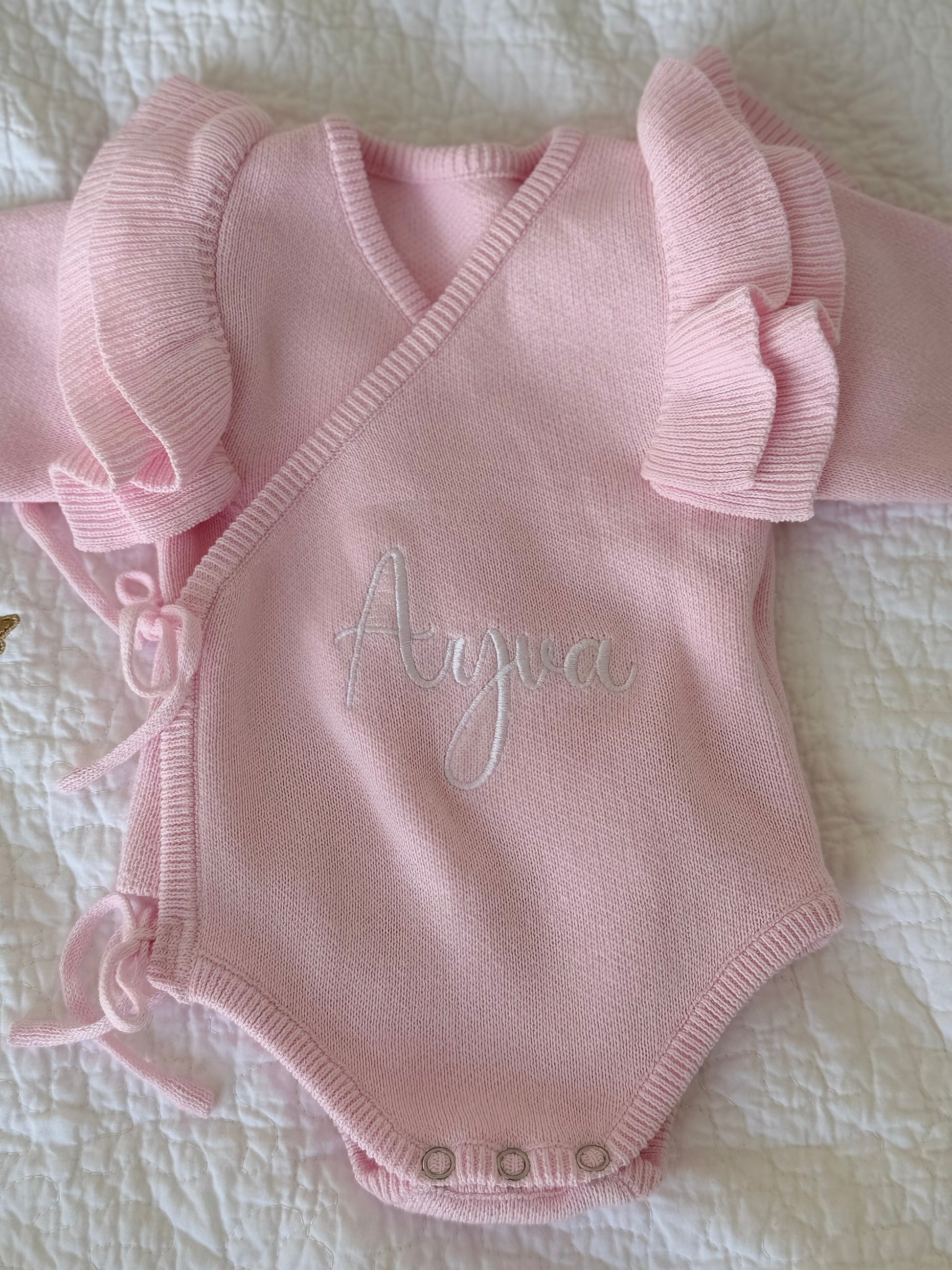 Personalised pink knit baby romper with sweet ruffle sleeves styled on quilt — Maxims Gift Co. nursery gift UAE
