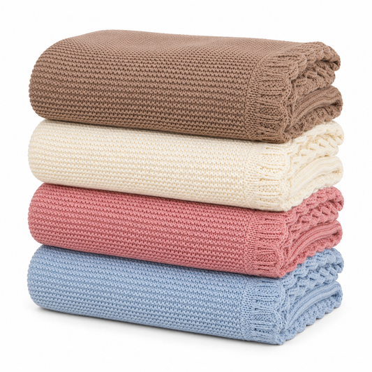 Stacked scalloped knitted baby blankets in brown, cream, blush pink and baby blue on a white background.